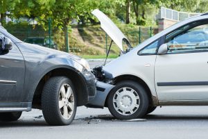 An image of two cars that have collided into each other front on. Both cars have damage to their bumper, one with considerably more damage with the hood up.